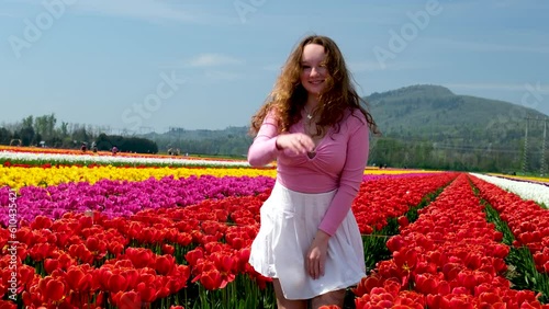 young girl woman twirling in red tulips in white tennis skirt pink blouse beautiful long hair brown-haired woman takes hand to side looks into distance tender young beauty virginity