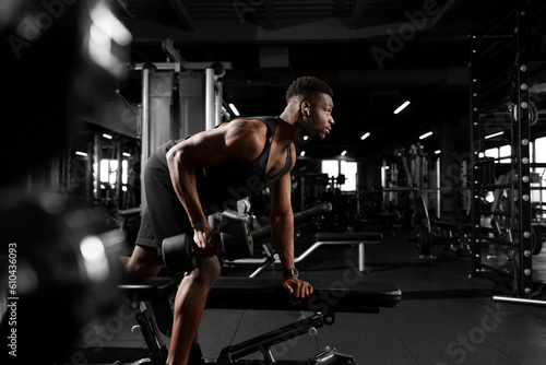 athletic african american man trains in dark gym, athletic guy lifts heavy dumbbells in fitness club