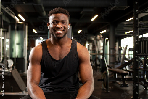 young athletic african american man sits in dark gym and smiles  athletic guy rests in fitness club