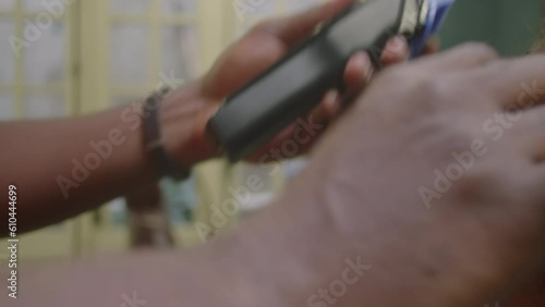Close-up impersonal shot of hands of barber using hair clippers and comb for trimming neckline of male client