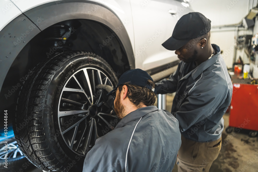Two men car mechanics at work, changing a car wheel of a lifted vehicle . High quality photo