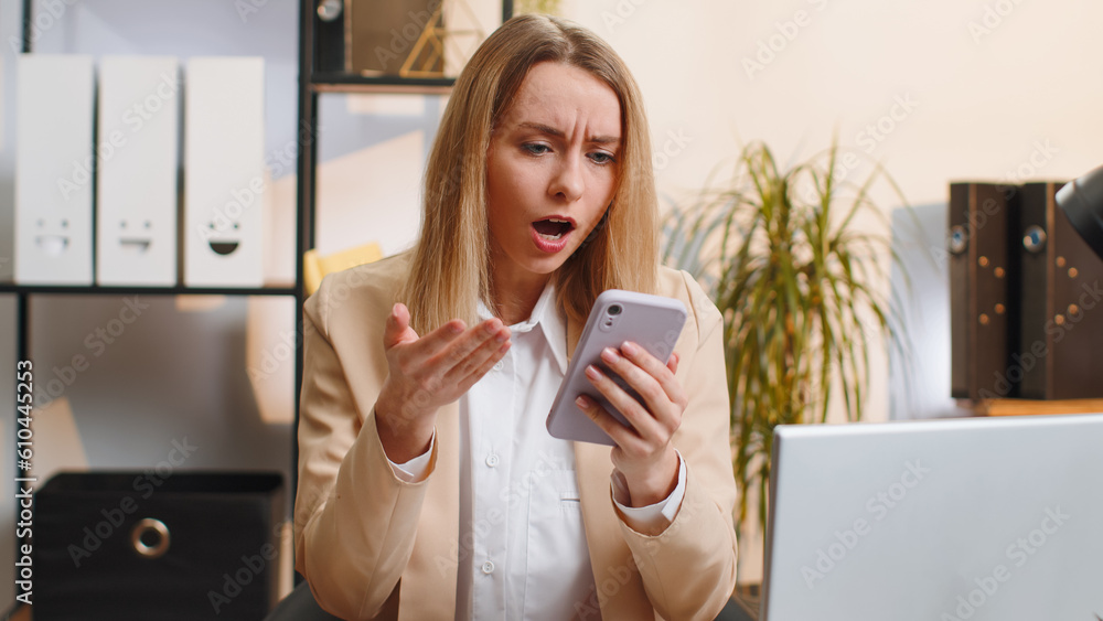 Young businesswoman in suit use smartphone typing browsing, loses becoming surprised sudden lottery results, bad news, fortune loss fail at home office desk workplace. Blonde freelancer worker woman Young businesswoman in suit use smartphone typing browsing, loses becoming surprised sudden lottery results, bad news, fortune loss fail at home office desk workplace. Blonde freelancer worker woman