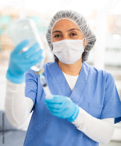 Female nurse in a protective mask  working in the clinic in the treatment room  fills a syringe with medicine with ..saline solution for injection