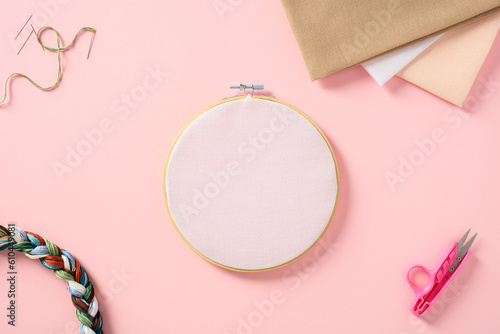 Embroidery hoop mockup on pink background with cross stitch accessories. Flat lay, top view. photo