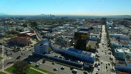 Aerial Panning Shot Of Vehicles On Street Amidst Buildings Against Sky, Drone Flying Over City On Sunny Day - Beverly Hills, California