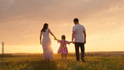 Parents, daughter run at sunset, kid holds hands of his parents and jumps. Active family playing in meadow with their daughter at sunset, teamwork. Happy family warm autumn day in park. Family, nature