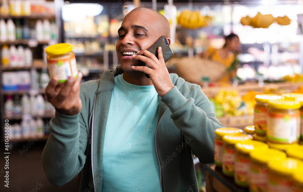 Positive man choosing canned food and talking on mobile phone in a grocery store
