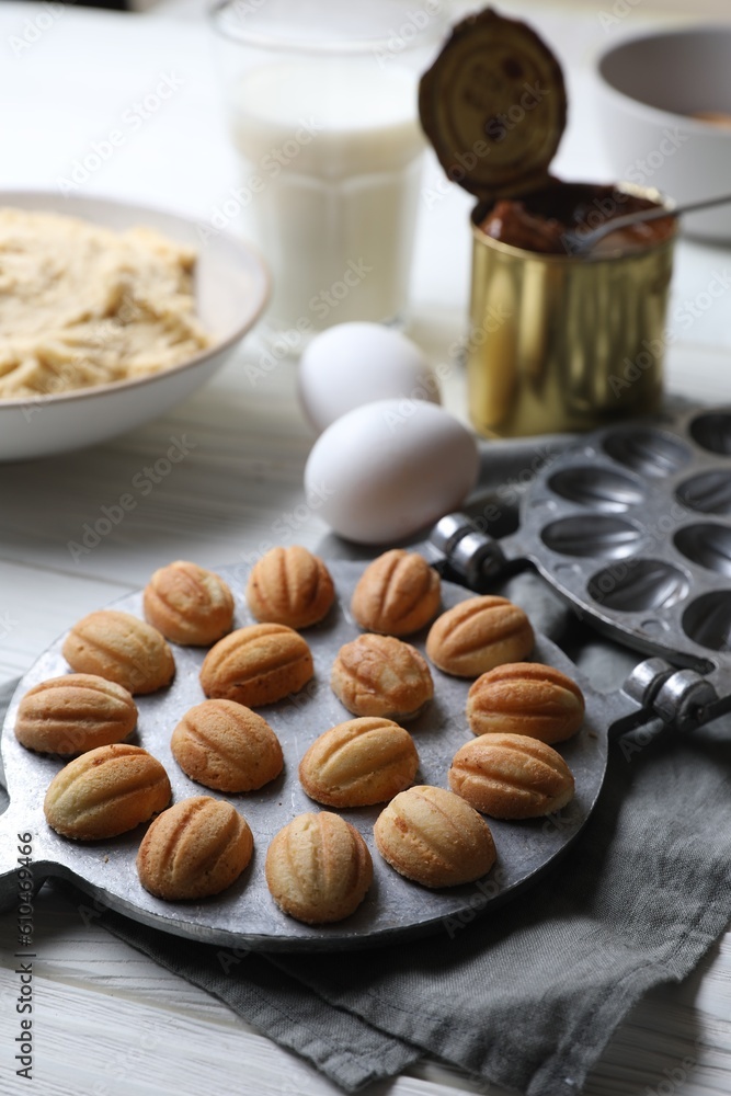 Delicious walnut shaped cookies with condensed milk and ingredients on white wooden table, closeup