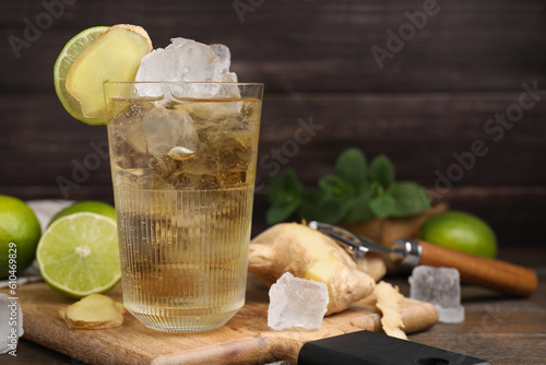 Glass of tasty ginger ale with ice cubes and ingredients on wooden table, space for text