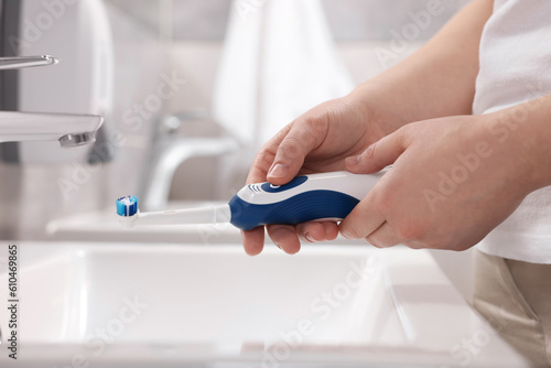 Woman holding electric toothbrush above sink in bathroom, closeup