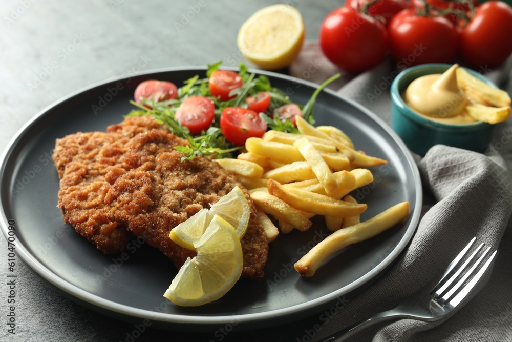 Tasty schnitzels served with potato fries, tomatoes and arugula on grey table, closeup Tasty schnitzels served with potato fries, tomatoes and arugula on grey table, closeup