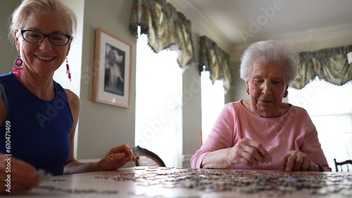 Obraz na plátně Smiling mature woman places puzzle piece while elderly lady moves puzzle pieces around