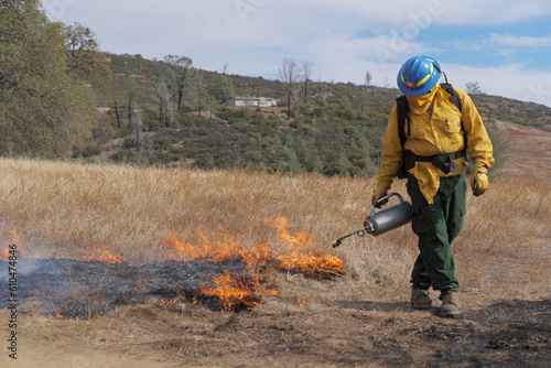 A firefighter lights grass on fire using a drip torch 