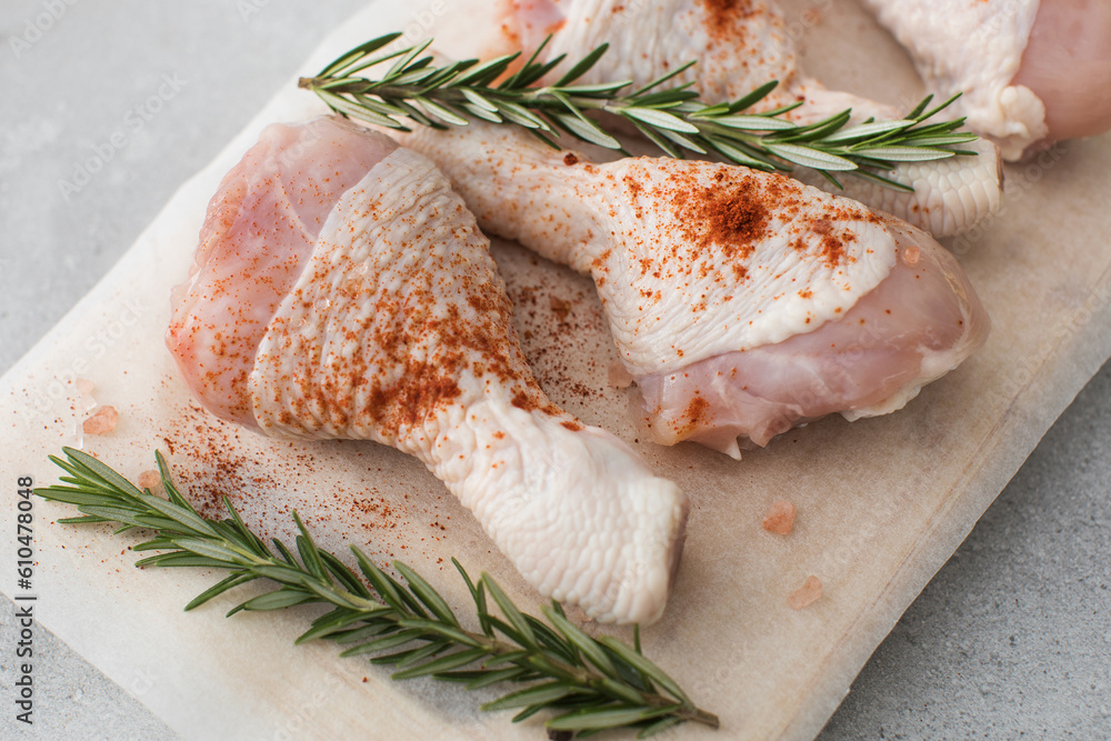 Raw chicken legs with spices and rosemary sprigs on a wooden cutting board. Raw chicken legs with spices and rosemary sprigs on a wooden cutting board.
