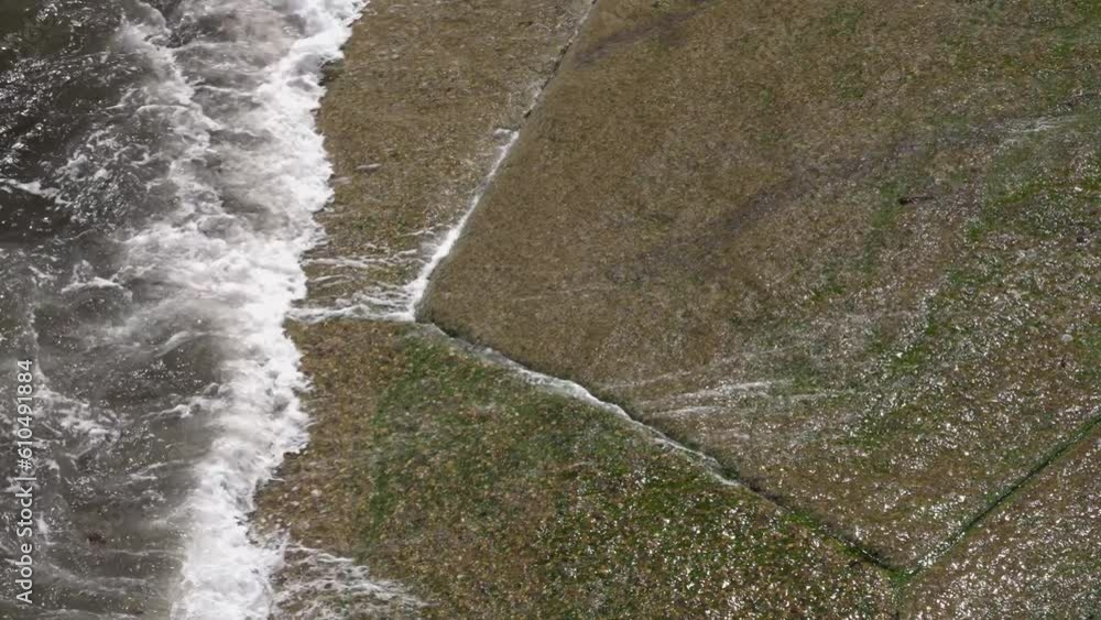 Close up of waves crashing on the boat ramp and causing small riptide with sea water flowing bac k under the new waves on stone shore Close up of waves crashing on the boat ramp and causing small riptide with sea water flowing bac k under the new waves on stone shore