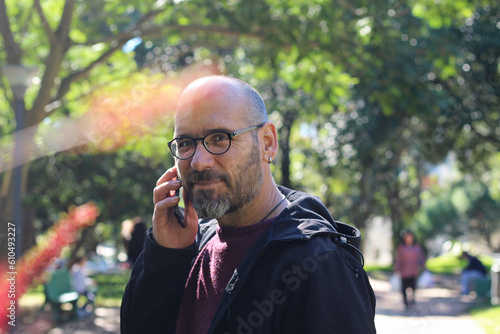 homem falando ao celular no parque da cidade em meio as árvores photo