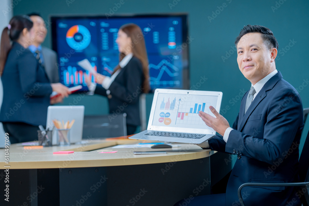Smiling middle-aged executive asian businessman sitting at a worktable a modern office, typing on computer keyboard, and talk to work, sending emails to his business partners, working on marketing. Smiling middle-aged executive asian businessman sitting at a worktable a modern office, typing on computer keyboard, and talk to work, sending emails to his business partners, working on marketing.