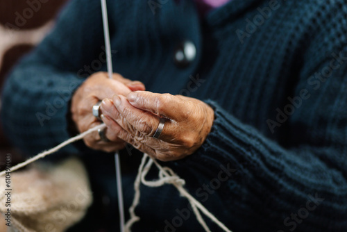 Abuela en la sala de casa feliz y concentrada, usando unos palitos de tejer y lana de oveja, concepto de vida cotidiana tradicional, tejedora tradicional, enfoque selectivo. Dia de los abuelos.