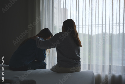 Silhouette image of a woman touching her friend shoulder to comforting and giving encouragement in bedroom