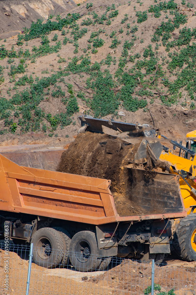 Obraz premium Loader pours earth into the dump truck body on a summer day