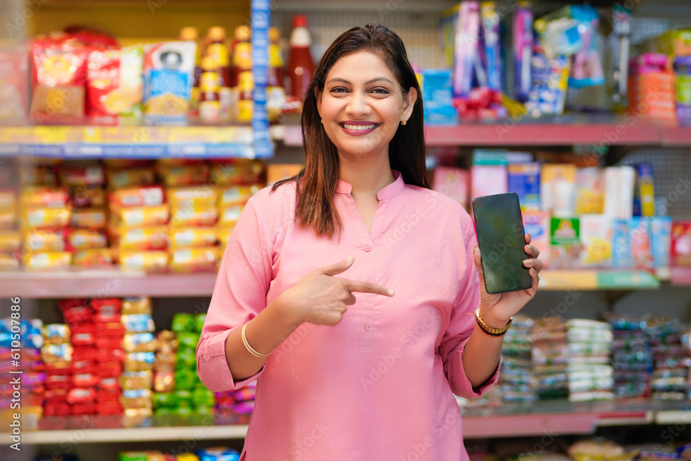 Indian woman showing smartphone screen at grocery shop.