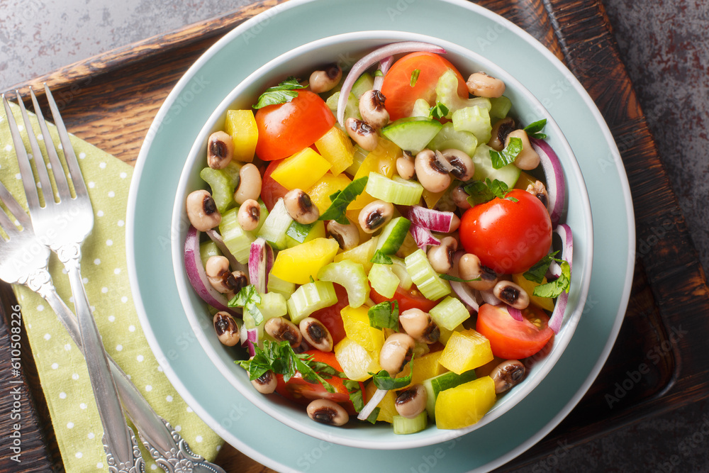 Summer salad with cherry tomatoes, celery, yellow pepper, black-eyed peas, cucumber and onion close-up in a bowl on a wooden board. horizontal top view from above