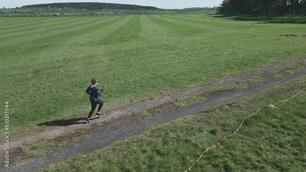 Drone dynamic shot of a woman jogging along a dirt road in a vast landscape. Drone dynamic shot of a woman jogging along a dirt road in a vast landscape.