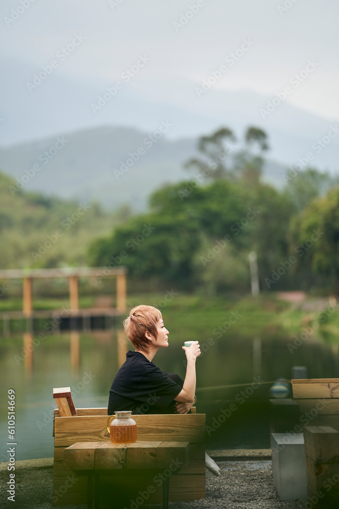 Asian beauty sitting beside pond breathing fresh air drinking tea