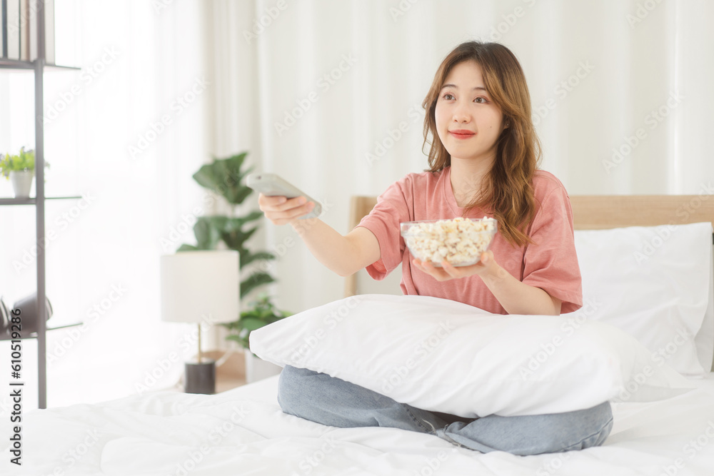 Asian woman using remote tv for watching online movie relax in bedroom with popcorn Asian woman using remote tv for watching online movie relax in bedroom with popcorn