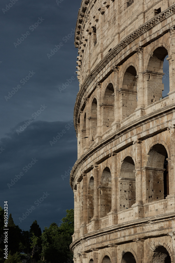 Close view of the Colosseum in Rome in front of a dark, cloudy sky.