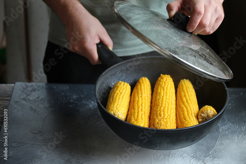 A man opening pan with roasted corn on the cob. Healthy food. 