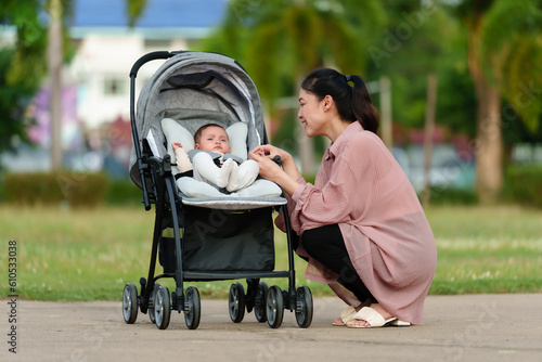 happy mother talking and playing with her infant baby in the stroller while resting in park photo