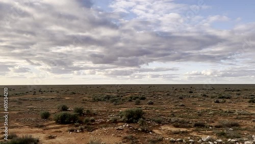 Indian Pacific Train travels through the vast, barren Western Australian Nullabor Plain on cloudy day. Low scrub & saltbush survives in red dirt photo