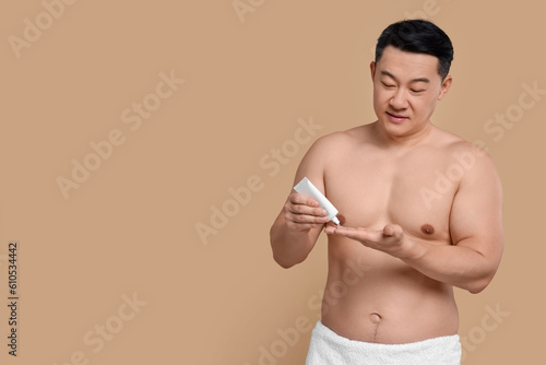 Handsome man applying body cream onto his hand on light brown background. Space for text
