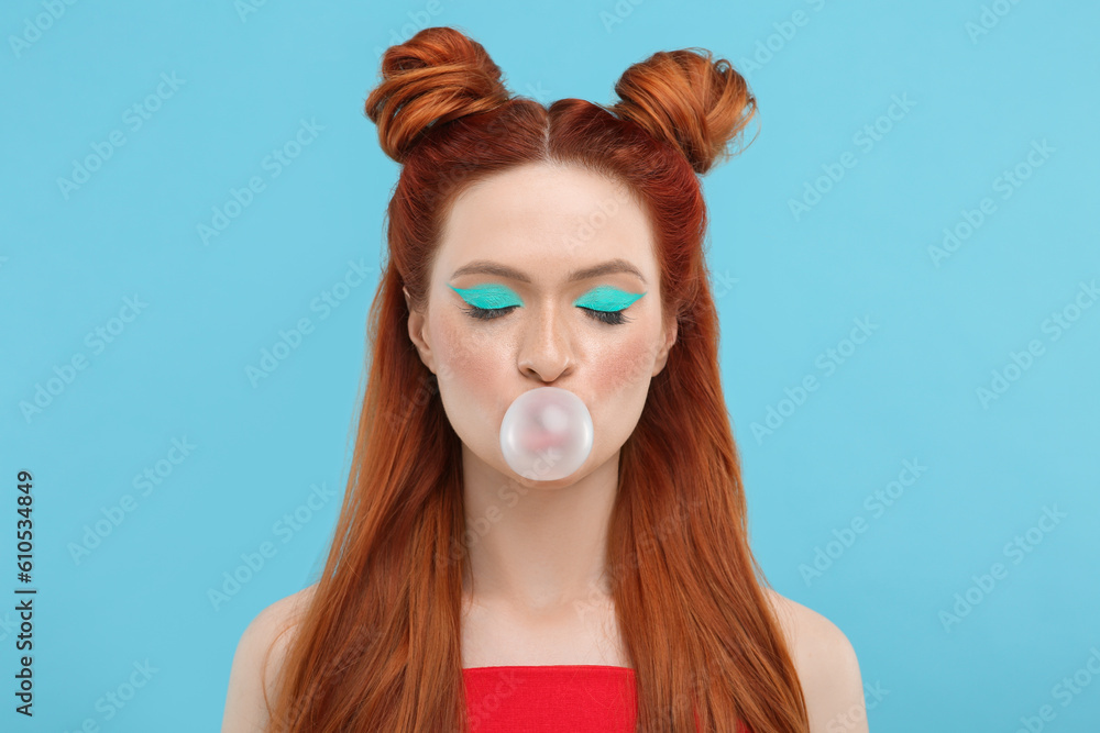 Naklejka premium Beautiful woman with bright makeup and closed eyes blowing bubble gum on light blue background