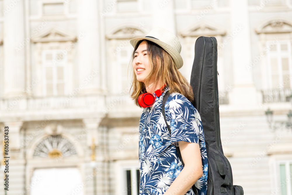 Happy young musician with guitar walking through city