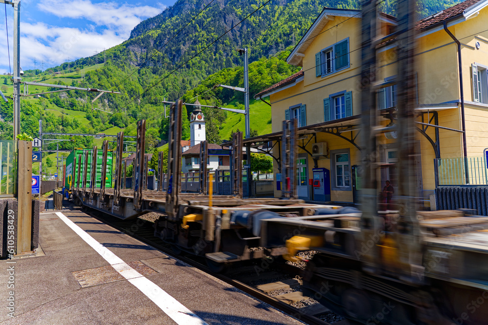 Freight train passing Swiss railway station Sisikon on a sunny spring noon. Photo taken May 22nd, 2023, Sisikon, Switzerland.