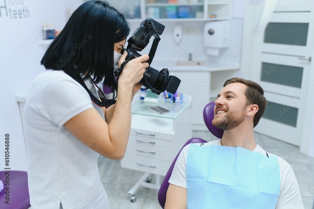 Fototapeta premium Handsome man smiling while teeth exam. Happy male patient sitting in a dentist's chair and having check up teeth.