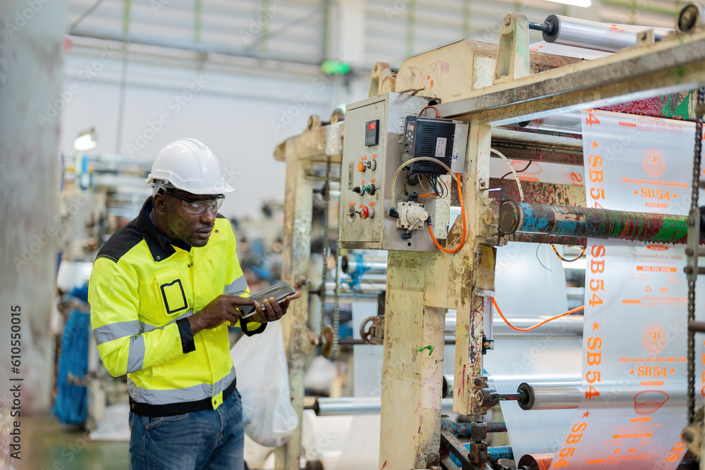 African male engineer manager is a mechanic Looking at steel and plastic production machines Control work with a tablet, wear a vest, and a helmet in a large business industry. African male engineer manager is a mechanic Looking at steel and plastic production machines Control work with a tablet, wear a vest, and a helmet in a large business industry.