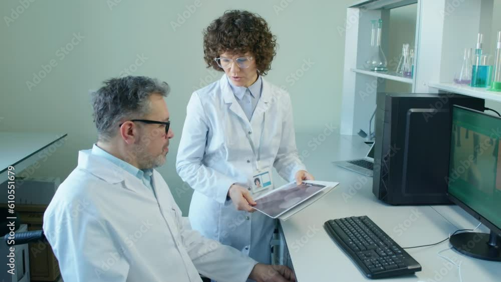 Medium high angle shot of female Caucasian assistant explaining something to professor in wheelchair in laboratory at daytimeMedium high angle shot of female Caucasian assistant explaining something t Medium high angle shot of female Caucasian assistant explaining something to professor in wheelchair in laboratory at daytimeMedium high angle shot of female Caucasian assistant explaining something t