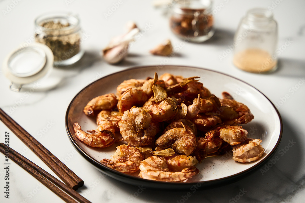 Crispy Pan fried tiger shrimps or prawns with garlic. Chinese or Asian cuisine dish. Shrimps lay on white plate on white marble background. T Crispy Pan fried tiger shrimps or prawns with garlic. Chinese or Asian cuisine dish. Shrimps lay on white plate on white marble background. T