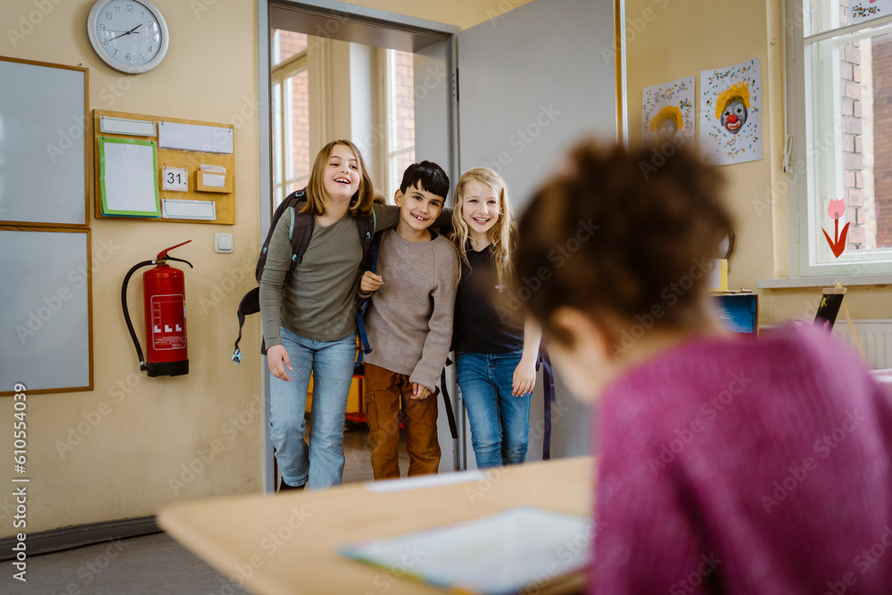 Happy friends with arms around each other entering classroom Happy friends with arms around each other entering classroom