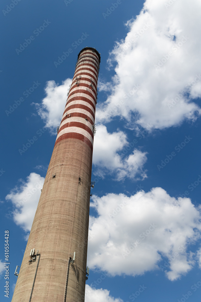 A mobile phone antennas installed on a tall power plant chimney. Object against the blue sky on a sunny day.