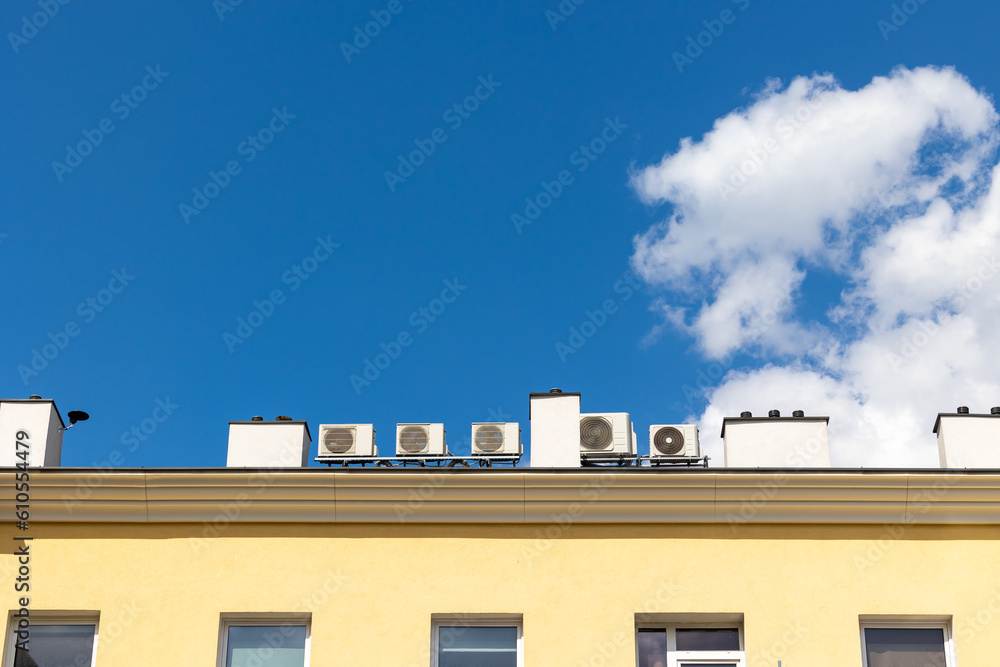 Many air conditioners on the roof of the building. Shot on a sunny day against a blue sky.