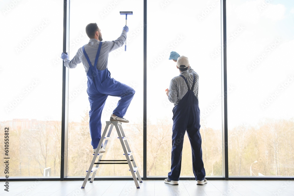 multiethnic professional cleaners in uniform washing large windows in office