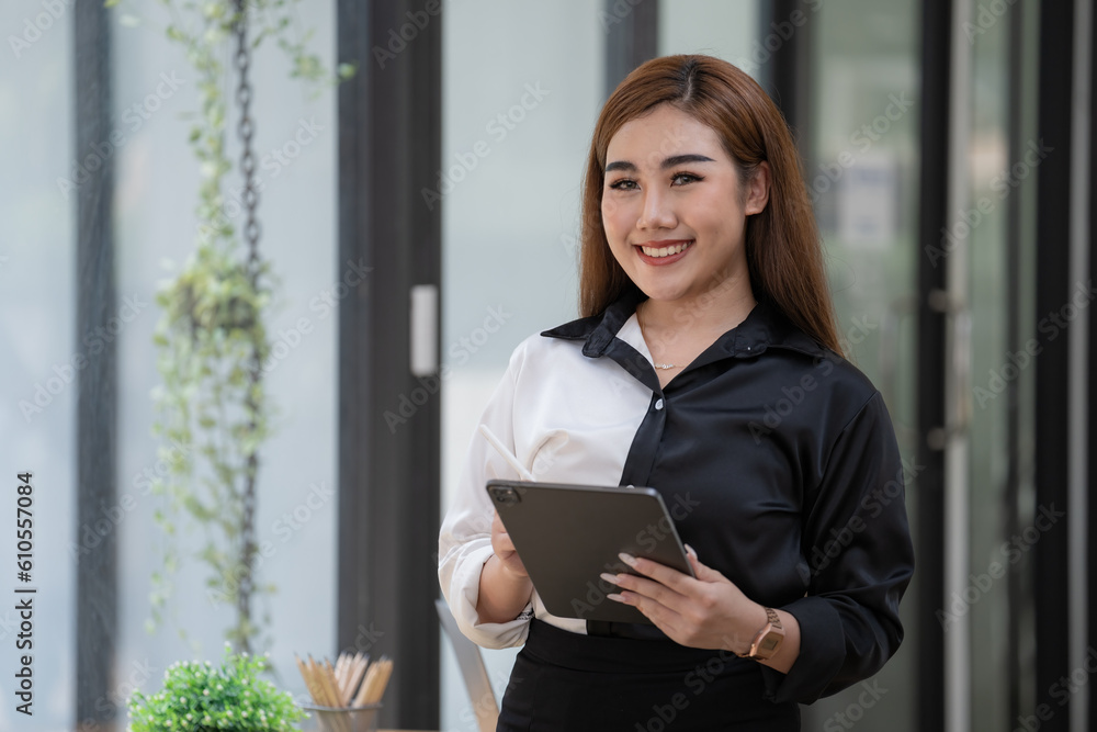 Fototapeta premium Smiling young Asian businesswoman holding a digital tablet standing in an office.