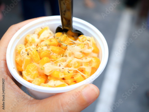 Corn and cheese in white cup with black plastic spoon.