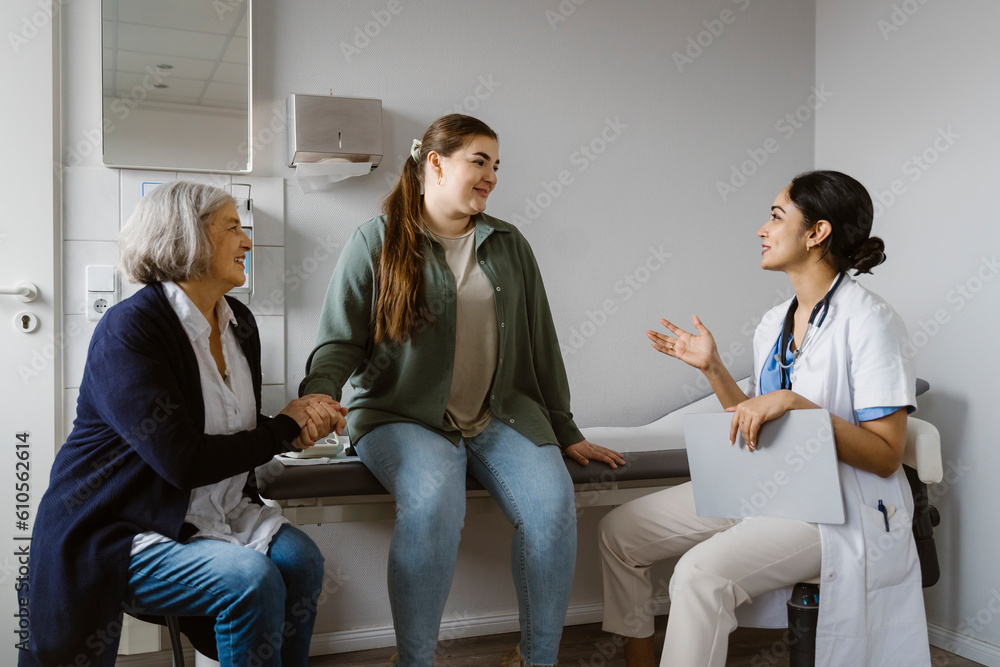 Female doctor explaining patient sitting with mother in clinic Female doctor explaining patient sitting with mother in clinic