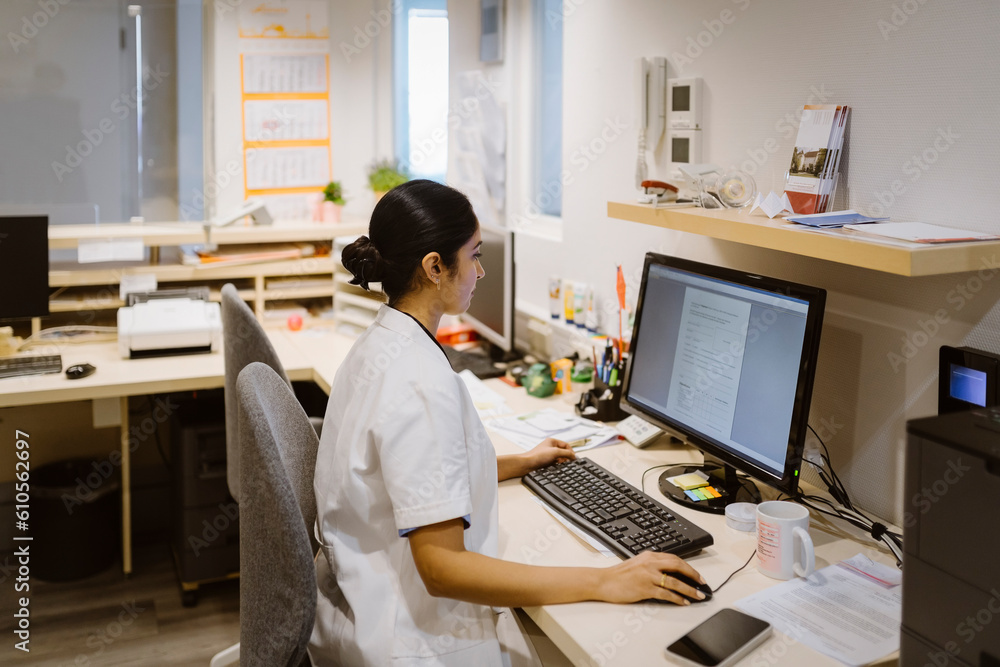 Side view of female healthcare worker using desktop PC at hospital Side view of female healthcare worker using desktop PC at hospital