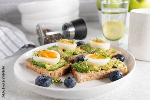 Breakfast toast with avocado spread  boiled eggs and cress on a plate. Served with a glass of water and coffee on a kitchen table.